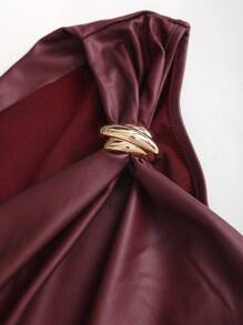 Close-up of the gold-tone ring detail gathering the burgundy faux leather shoulder into an elegant draped asymmetric shape.