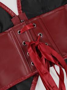 A close-up of a red faux leather corset-style harness with red satin laces threaded through silver metal eyelets, shown against a black and white background.