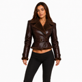 A woman modeling a dark brown faux-shearling leather jacket with a belted waist and collar, paired with black pants, against a plain white background.