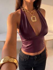 Front view of a black faux leather halter crop top with a deep V-neckline, gathered bust panels and fitted waist, styled with jeans.