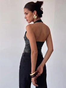 Back view of a black faux leather halter crop top showing the neck strap, open upper back and fitted lower panel, worn with dark jeans.